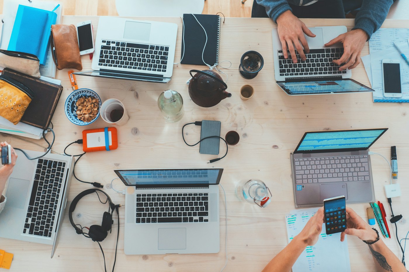 Mesa vista desde arriba con varias laptops, libretas y objetos de trabajo