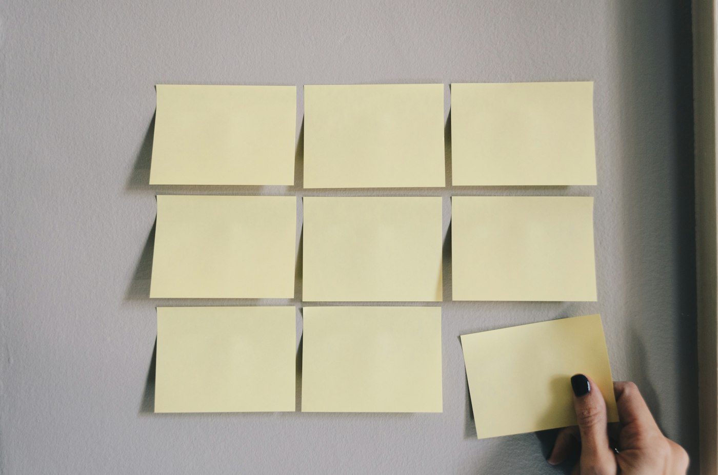 Notas adhesivas amarillas en blanco sobre una pared, una mano colocando la última